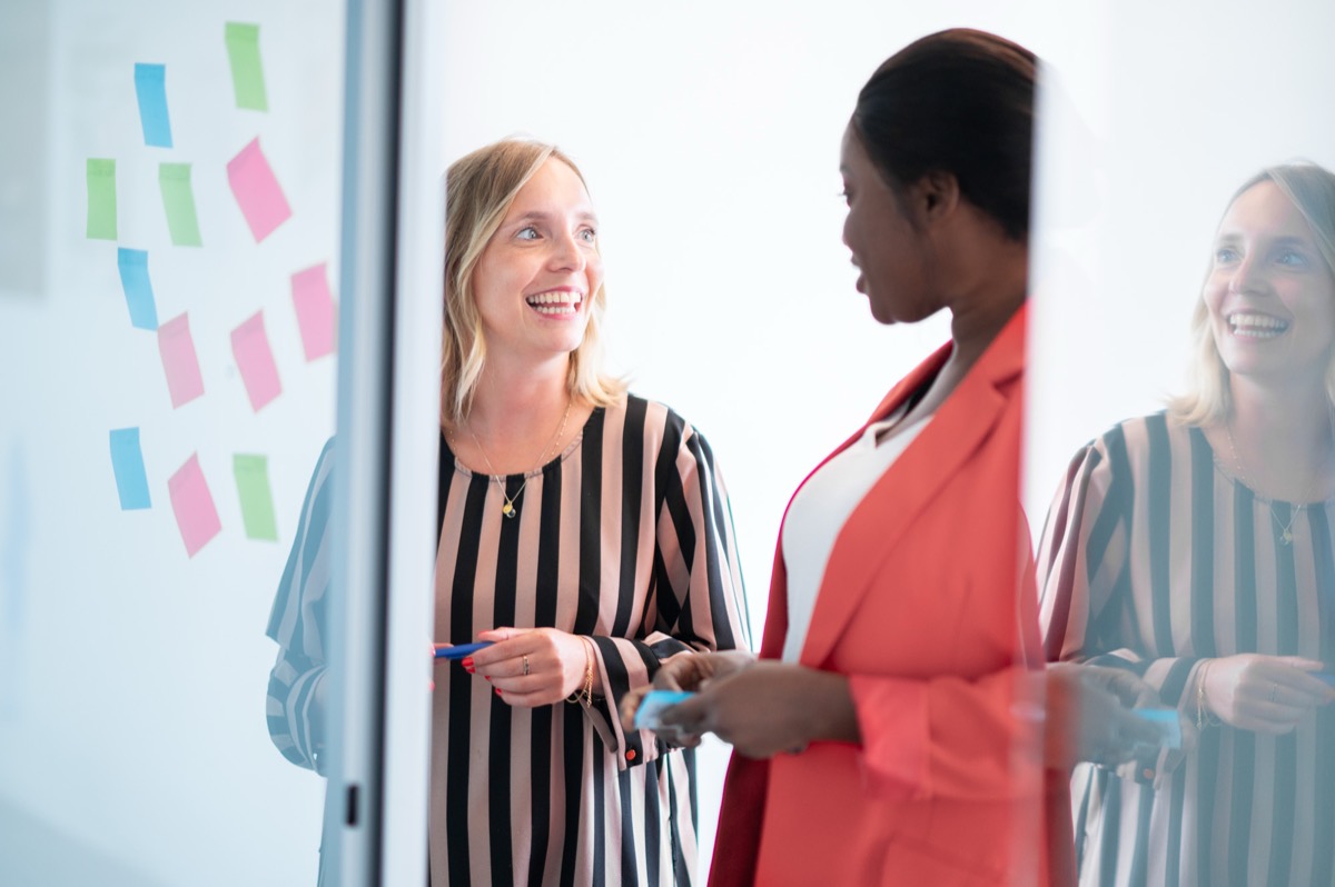 Twee collega's in gesprek naast een glazen wand vol kleurige post-its.